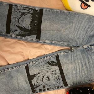 May include: A pair of blue denim jeans with black and white anime illustrations painted on the legs.