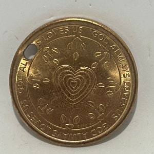 May include: Gold-colored metal token with the words "God Always Loves Us" and "God Always Loves Us" inscribed around a heart design.