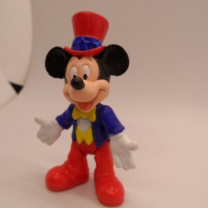 May include: A red, white, and blue Mickey Mouse figurine wearing a red, white, and blue Uncle Sam hat. The figurine is made of plastic and has a yellow bow tie.