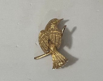 May include: A gold-toned bird brooch with detailed textured wings and a delicate branch.