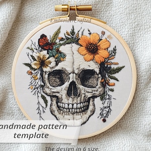 Puede incluir: Diseño de calavera bordada en un aro de madera. La calavera está adornada con flores y follaje coloridos. El texto "Handmade pattern template" y "The design in 6 size" son visibles. El aro mide unos 15 cm de diámetro.