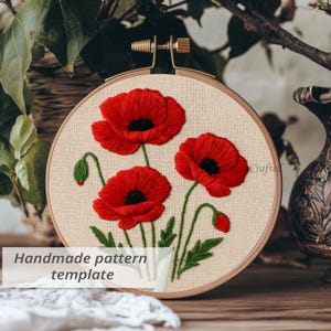 May include: An embroidery hoop featuring a handmade pattern of red poppies with black centers and green stems and leaves. The embroidery is set against a beige fabric background. The text "Handmade pattern template" is visible.