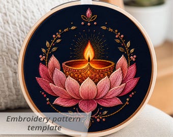 May include: Embroidered artwork in a wooden hoop. The design features a lotus flower with a lit diya lamp at the center, surrounded by gold-colored leaves and a dark blue background. Text at the bottom reads "Embroidery pattern template."