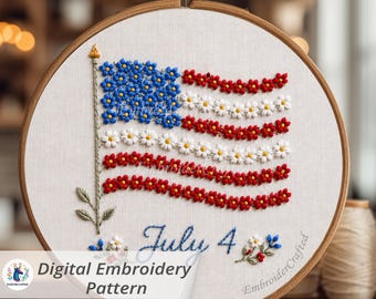 May include: A circular wooden embroidery hoop containing a white fabric panel with a hand-stitched design of an American flag made from small blue, white, and red flowers. The text July 4 is embroidered in blue script below the flag design.