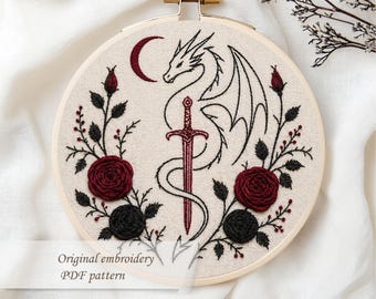 May include: Embroidered hoop art featuring a dragon, sword, and crescent moon design. The artwork includes red and black roses and the text "Original embroidery PDF pattern". The embroidery is set in a wooden hoop.