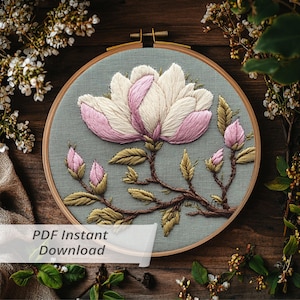 Puede incluir: Bordado a mano de una flor de magnolia en un aro de madera. La flor tiene pétalos blancos y rosas, hojas verdes y tallos marrones. El texto "PDF Instant Download" es visible.