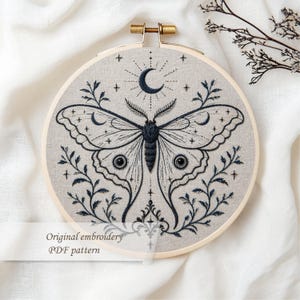 May include: Embroidered artwork in a wooden hoop features a detailed moth design with a crescent moon and stars. The moth is dark blue, and the background is a light beige fabric. Text on the image reads "Original embroidery PDF pattern."