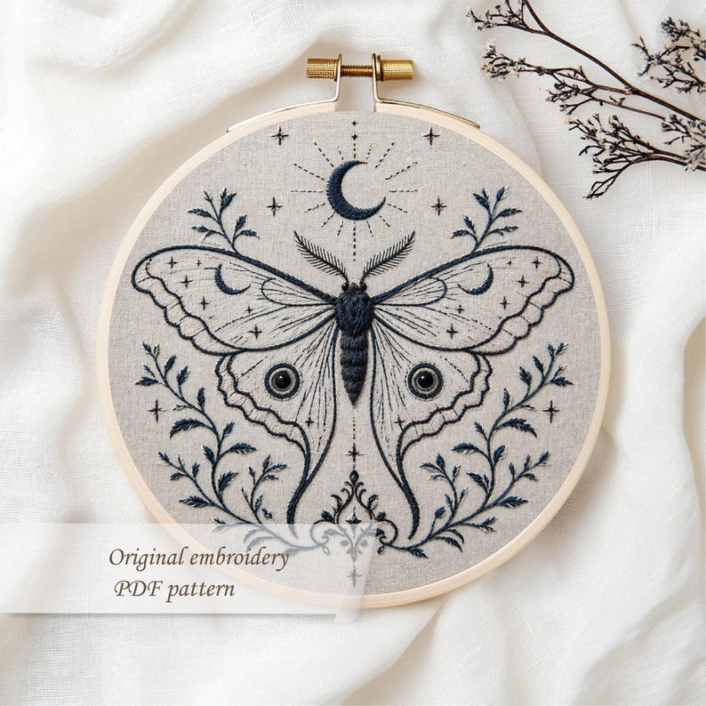 May include: Embroidered artwork in a wooden hoop features a detailed moth design with a crescent moon and stars. The moth is dark blue, and the background is a light beige fabric. Text on the image reads "Original embroidery PDF pattern."