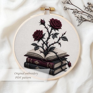 May include: Embroidered design of burgundy roses and thorns emerging from a stack of books. The embroidery is set in a wooden hoop. The text "Original embroidery PDF pattern" is at the bottom.