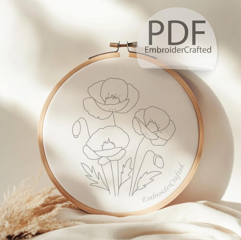 May include: A round embroidery hoop with a cream-colored fabric featuring a gray outline of poppy flowers. The wooden hoop has a metal clasp. The text "PDF EmbroiderCrafted" is visible.