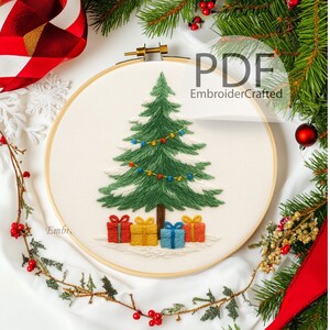 Puede incluir: Árbol de Navidad bordado en un aro de madera. El árbol es verde con detalles blancos, luces de colores y regalos en la base. El texto "PDF EmbroiderCrafted" es visible. Decoración festiva navideña.