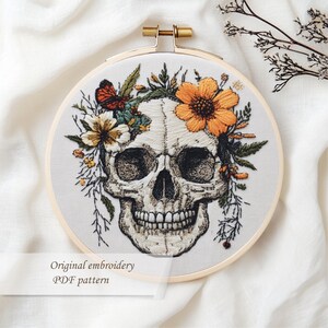 May include: Embroidered skull design in a wooden hoop. The skull is adorned with orange and yellow flowers, green leaves, and a butterfly. The text "Original embroidery PDF pattern" is at the bottom.
