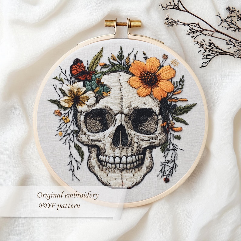 May include: Embroidered skull design in a wooden hoop. The skull is adorned with orange and yellow flowers, green leaves, and a butterfly. The text "Original embroidery PDF pattern" is at the bottom.
