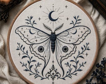 May include: Embroidered artwork in a wooden hoop features a detailed moth design with a crescent moon and star accents. The moth is dark blue, with intricate wing patterns and surrounded by floral elements. The background is a light beige fabric.