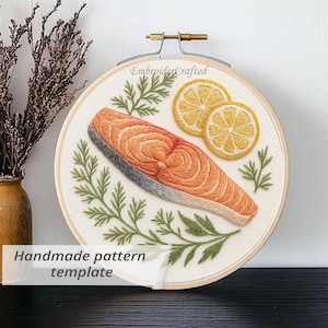 Op de afbeelding: Geborduurde afbeelding van een zalmsteak, twee citroenschijfjes en dille in een houten borduurring. De tekst "EmbroiderCrafted" is zichtbaar. De tekst "Handmade pattern template" staat onderaan.