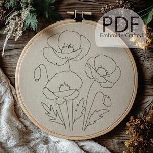 May include: A beige fabric stretched within a wooden embroidery hoop, featuring a detailed outline of three poppy flowers and buds. The design is in dark gray, with the text "PDF EmbroiderCrafted" in the upper right corner.