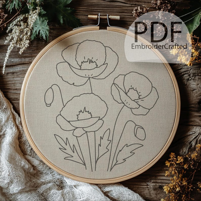 May include: A beige fabric stretched within a wooden embroidery hoop, featuring a detailed outline of three poppy flowers and buds. The design is in dark gray, with the text "PDF EmbroiderCrafted" in the upper right corner.