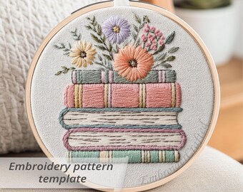 May include: A round embroidery hoop featuring a stack of embroidered books with colorful floral accents. The design includes a variety of flowers in shades of peach, lavender, and yellow. The text "Embroidery pattern template" is visible at the bottom.