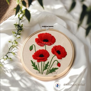 May include: A handcrafted embroidery hoop featuring three vibrant red poppy flowers with black centers and green leaves. The floral design is set against a beige fabric background, framed by a wooden hoop. The text "EmbroiderCrafted" is visible.