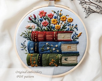 May include: Embroidered hoop art featuring a stack of three books with colorful floral arrangements. The books are in shades of red, blue, and green, with detailed stitching. The text "Original embroidery PDF pattern" is at the bottom.