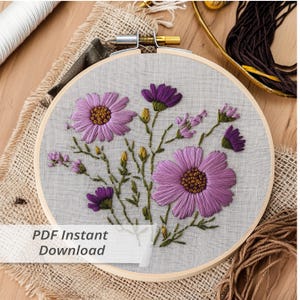 May include: A close-up of a finished embroidery hoop with a design of purple flowers on a gray fabric. The hoop is made of wood and has a natural finish. The text "PDF Instant Download" is visible at the bottom of the image.