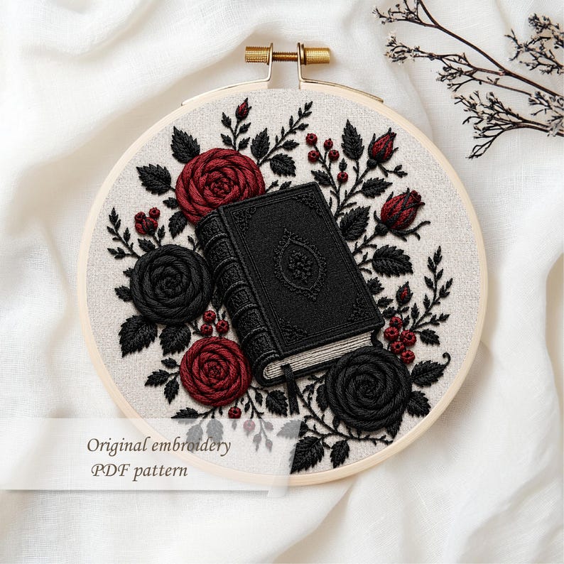 May include: Embroidered hoop art featuring a black book with ornate detailing, surrounded by red and black roses, leaves, and berries. The text "Original embroidery PDF pattern" is displayed at the bottom. The embroidery is set in a wooden hoop.