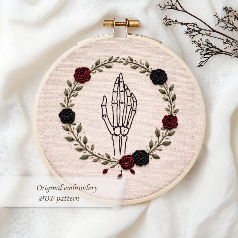 May include: An embroidery hoop featuring a skeletal hand design at the center, surrounded by a wreath of green leaves and alternating black and burgundy roses. The text "Original embroidery PDF pattern" is displayed at the bottom.
