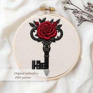 May include: An embroidery hoop featuring a black key design topped with a red rose and smaller red buds, surrounded by black leaves. The text "Original embroidery PDF pattern" is below the key.
