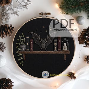 May include: Embroidered black hoop art featuring a bat with outstretched wings above a shelf with books and a potted plant. The text "PDF EmbroiderCrafted" is visible. The design includes stars and a crescent moon.
