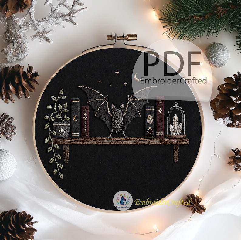 May include: Embroidered black hoop art featuring a bat with outstretched wings above a shelf with books and a potted plant. The text "PDF EmbroiderCrafted" is visible. The design includes stars and a crescent moon.