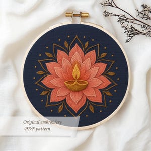 May include: Embroidered artwork in a wooden hoop. The design features a lotus flower with a central diya lamp, in shades of coral, gold, and navy blue. The text "Original embroidery PDF pattern" is visible at the bottom.
