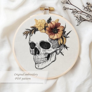 May include: An embroidery hoop featuring a detailed skull design adorned with a floral crown in shades of yellow and orange. The text "Original embroidery PDF pattern" is displayed at the bottom.