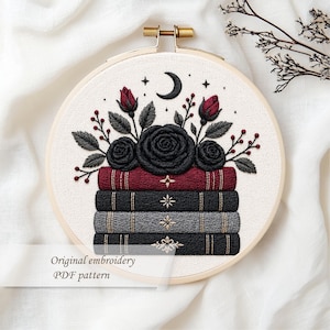 May include: Embroidered hoop art featuring a stack of books with a floral arrangement. The flowers are black roses and red buds, with gray leaves and berries. The books are burgundy, black, and gray. The text reads "Original embroidery PDF pattern."