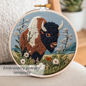 May include: A round embroidery hoop featuring a detailed bison design. The bison is depicted with brown, black, and white fur, set against a blue background with floral accents. The text "Embroidery pattern template" is visible.