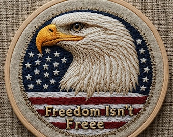May include: Embroidered hoop art featuring a detailed bald eagle head with a yellow beak and piercing eye. The design incorporates the American flag with blue, white stars, and red and white stripes. The text "Freedom Isn't Freeee" is stitched below.
