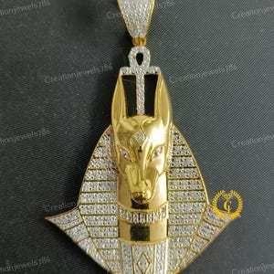 May include: Gold pendant featuring an Anubis head with a diamond-encrusted design. The pendant is in the shape of a pyramid with an Ankh symbol at the top.