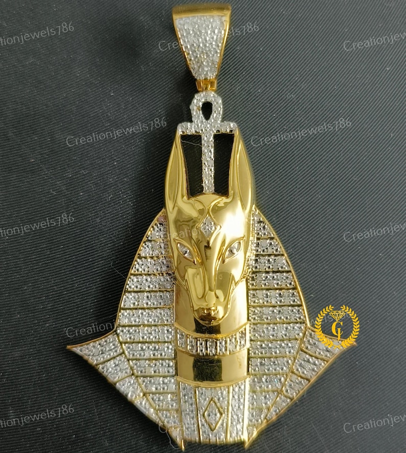May include: Gold pendant featuring an Anubis head with a diamond-encrusted design. The pendant is in the shape of a pyramid with an Ankh symbol at the top.