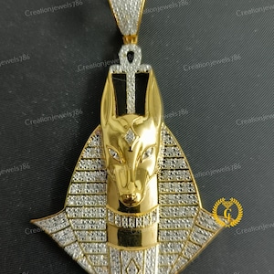 May include: Gold pendant featuring an Anubis head with a diamond-encrusted collar and an ankh symbol at the top. The pendant is made of gold and has a shiny finish.