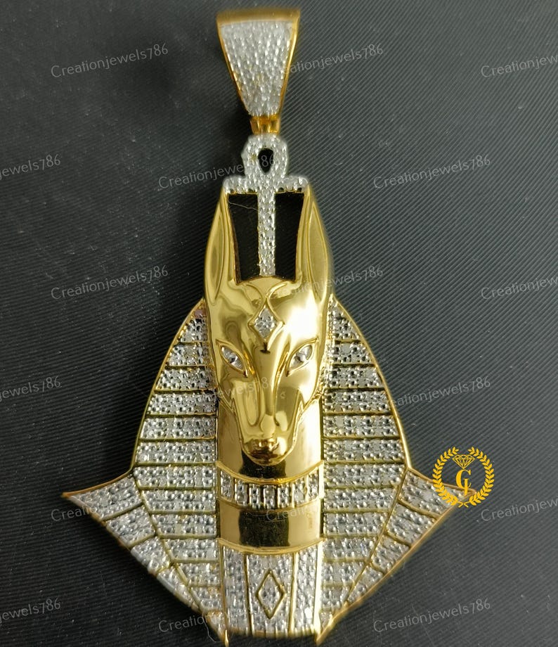 May include: Gold pendant featuring an Anubis head with a diamond-encrusted collar and an ankh symbol at the top. The pendant is made of gold and has a shiny finish.