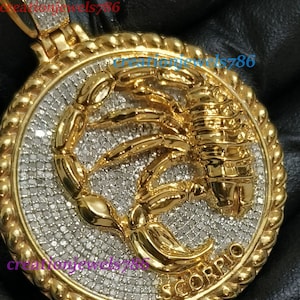 May include: Gold pendant with a scorpion design, set with clear diamonds and the word "SCORPIO" inscribed around the edge.