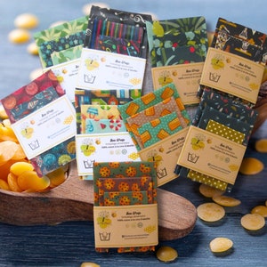 Peut inclure: Assortiment d'emballages alimentaires en cire d'abeille colorés avec différents motifs et designs. Les emballages sont conditionnés par lots de trois et présentent un logo avec le texte "Bee Wrap".