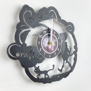 May include: A black vinyl record clock featuring a silhouette of a girl and a cat, with the words "Coraline" written on the clock face. The clock face has a white background with black numbers and a black and white moon design.