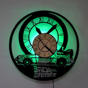 May include: A black vinyl record clock with a green light behind it. The clock features a silhouette of the DeLorean time machine from the movie Back to the Future. The clock also has the words "Back to the Future" printed on it.