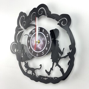 May include: Black vinyl record clock featuring a silhouette of Coraline from the movie Coraline, a black cat, and a clock face with white numbers and gold hands.