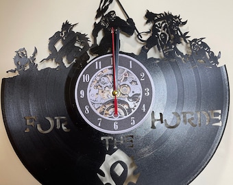 Puede incluir: Un reloj de vinilo negro con una esfera de reloj y una silueta de orcos del videojuego World of Warcraft. La esfera del reloj tiene el texto "FOR THE HORDE" y el símbolo de la Horda.