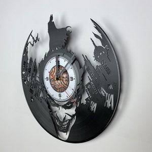 May include: Black vinyl record clock featuring a Joker silhouette with a clock face in the center. The clock face has Roman numerals and a red second hand. The background of the clock is black with a white silhouette of a city skyline and the word "HAHAHA" in white.