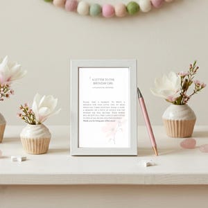 May include: A white picture frame containing a printed card titled A Letter to the Birthday Girl, with text inviting guests to write a message. A pink pen rests against the frame, flanked by four ceramic cupcake-shaped vases holding white flowers.