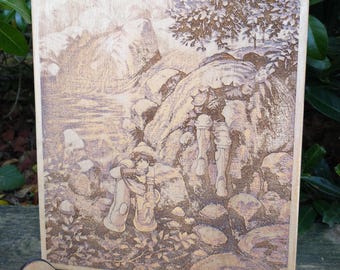 May include: A wooden plaque with an engraved landscape scene, depicting figures, rocks, and trees. The artwork is displayed on a wooden easel. The colour is light brown.