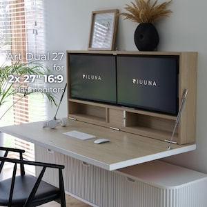 Op de afbeelding: Een licht houten bureau met twee 68,58 cm flatscreen monitoren. Het bureau heeft een neerklapbaar werkoppervlak en een witte kastvoet. De tekst "Art Dual 27 for 2x 27" 16:9 flat monitors" is zichtbaar.