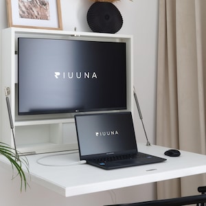 Pode incluir: Uma secretária branca dobrável montada na parede com uma superfície plana, uma prateleira integrada e dois suportes metálicos. Um monitor preto e um portátil preto, ambos com o texto IUUNA, estão colocados na secretária com um rato preto.
